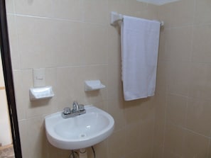 Un baño con un lavamanos blanco, una toalla colgada en un perchero y un jabonera.