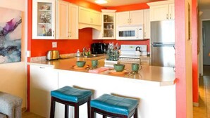 Une cuisine avec des meubles blancs, un îlot central doté de tabourets et un mur d’accent rouge.