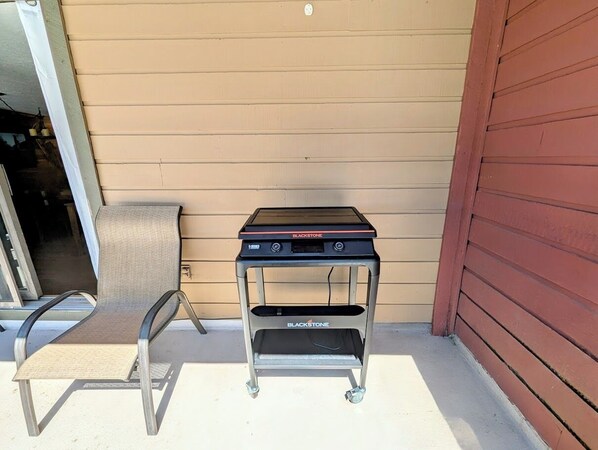A grill cart with a chair beside it, positioned against a house wall.