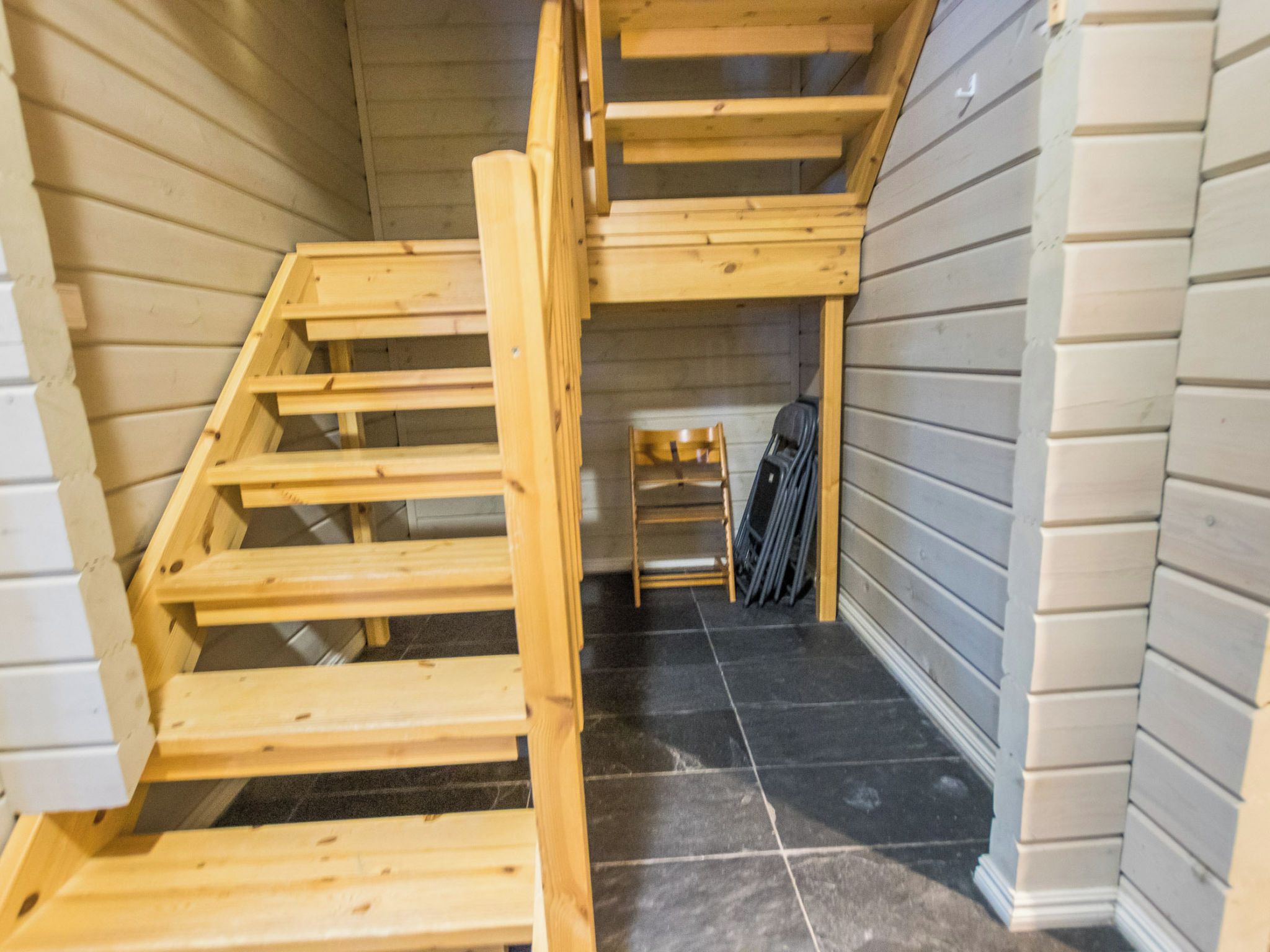 Un escalier en bois menant à une mezzanine aménagée avec une chaise et une valise.