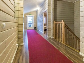 A hallway with a red carpet, wooden walls, and a wooden railing on the right. - Vacation home  by Interhome (Hyrynsalmi)