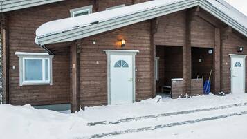 Una cabaña de madera con techo nevado, una puerta principal y una ventana.