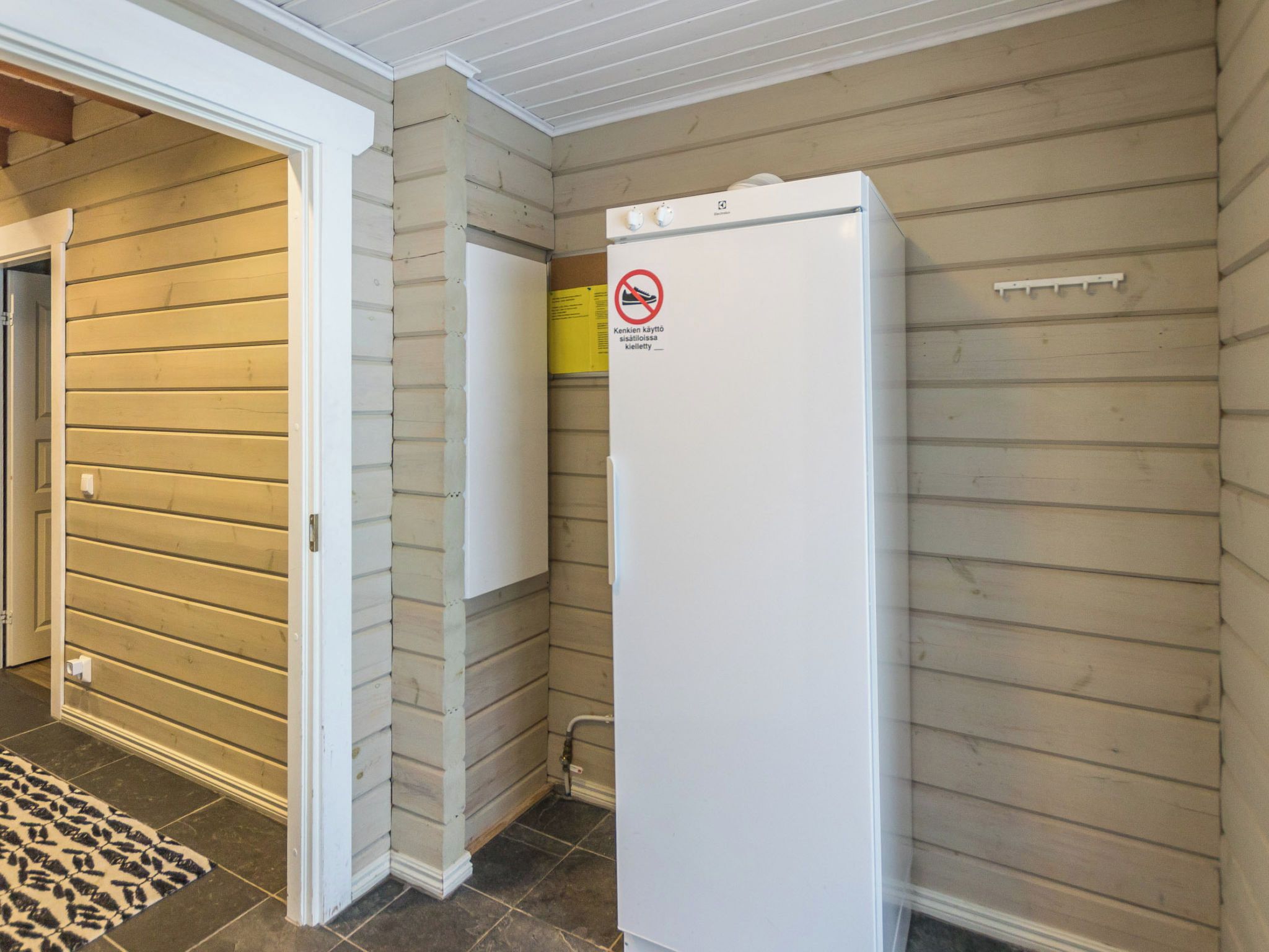 A compact kitchen with a white refrigerator, wooden walls, and a yellow sign.