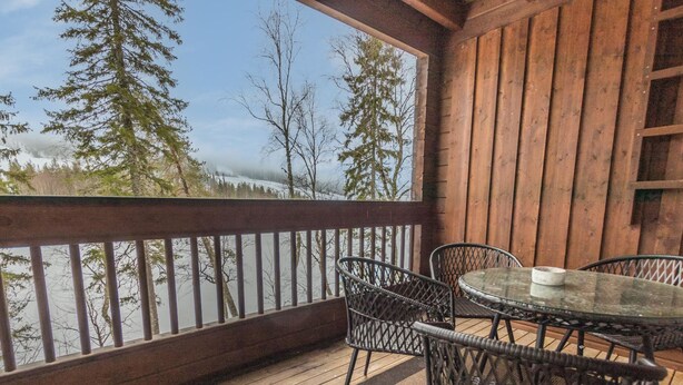 A wooden deck with a glass table and chairs, overlooking a forested area with trees and a view of a mountain range. - Uulanlinna a, paritalo by Interhome (Hyrynsalmi)