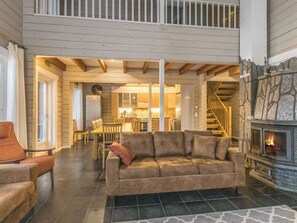 A spacious living area with a high ceiling, a fireplace, and a staircase leading to an upper level. - Uulanlinna a, paritalo by Interhome (Hyrynsalmi)