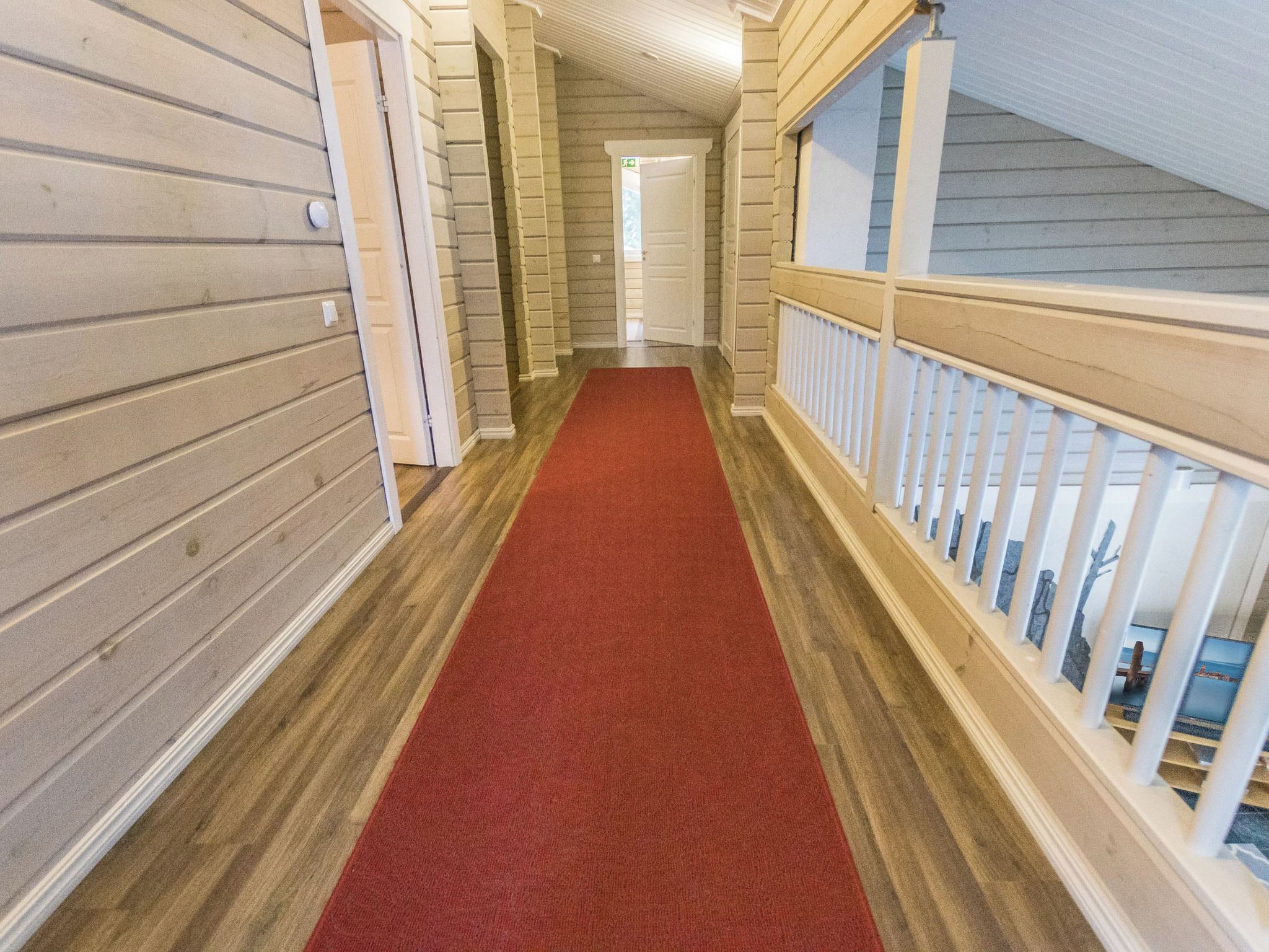 Un couloir avec un tapis rouge, des murs en bois et une rambarde blanche sur le côté droit.