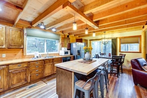 A spacious kitchen with wooden cabinets, a central island, and a dining area with a red leather couch. - Peaceful Garden Valley Cabin w/ Private Deck! (Garden Valley)