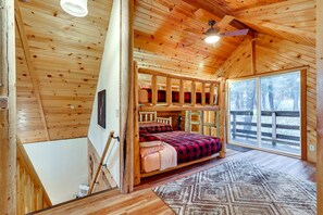 A cabin with a loft bed, a large window, and a wooden interior. - Peaceful Garden Valley Cabin w/ Private Deck! (Garden Valley)