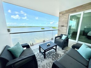 A balcony with a view of a body of water, wicker furniture, and a glass door.