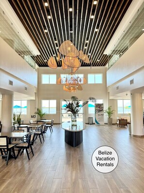 A spacious lobby with a high ceiling, modern pendant lighting, and large windows offering views of the outdoors.