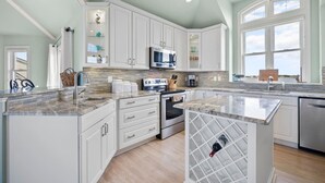A modern kitchen with white cabinets, a stainless steel oven, and a large island with a wine cooler. - Compass Tres: Guiding You To Vacation Perfection! (North Topsail Beach)