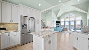 A spacious kitchen with white cabinetry, a stainless steel refrigerator, and a marble countertop island. - Compass Tres: Guiding You To Vacation Perfection! (North Topsail Beach)