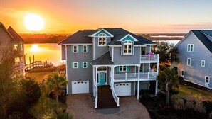 A two-story house with a balcony, a front porch, and a view of the sunset over water. - Compass Tres: Guiding You To Vacation Perfection! (North Topsail Beach)