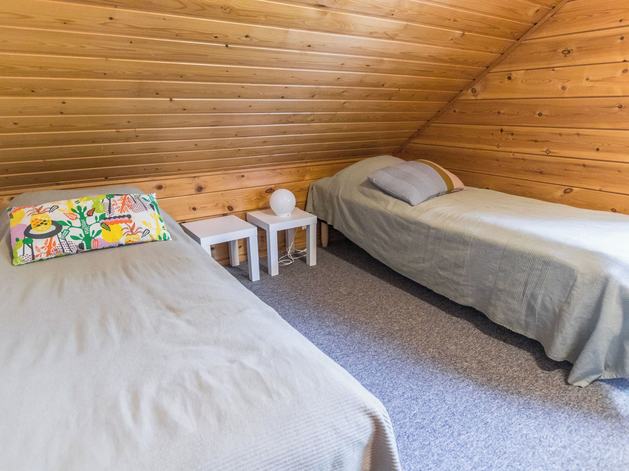 A small, cozy room with two beds, a small table, and a colorful pillow.