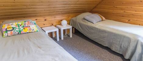 A small, cozy room with two beds, a small table, and a colorful pillow.