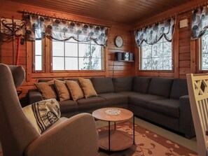 A cozy cabin interior with a sectional sofa, a round coffee table, and a television mounted on the wall.