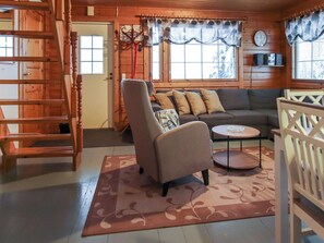 A cozy cabin interior with a wooden staircase, a sofa set, a round table, and a patterned rug.