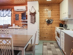 A cozy cabin-style kitchen with wooden walls, a dining area with a table and chairs, and a refrigerator.