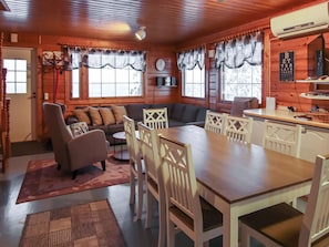 A cozy cabin interior with a dining table, chairs, a sofa, and a kitchen area.