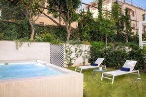 Un área de piscina privada con un jacuzzi, dos sillones de descanso y una pequeña mesa.