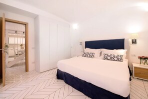 A bedroom with a bed, a nightstand, a lamp, and a door leading to a bathroom.