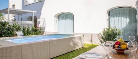A modern outdoor pool area with a wooden deck, a dining table set with plates and glasses, and a fruit bowl.