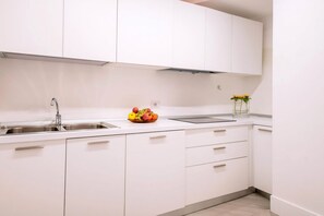 Una cocina moderna con armarios blancos, un lavamanos de acero inoxidable y un bol de frutas en la encimera.