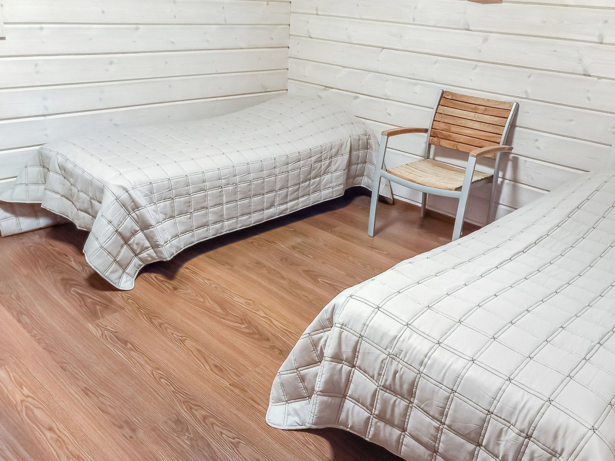 Una stanza con due letti, una sedia di legno e un muro bianco.