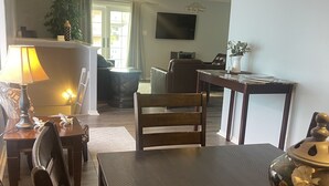 Een eetgedeelte met een houten tafel, stoelen en een decoratieve schaal. Een televisie is aan de muur bevestigd en er staat een plant op de achtergrond.