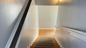Een trap met houten treden en witte leuningen, die uitkomt op een plateau met een lamp.