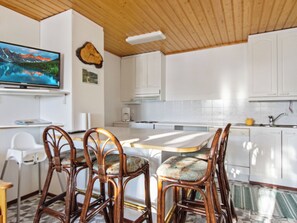 Una cocina moderna con armarios blancos, una mesa de comedor con sillas y un televisor de pantalla plana en la pared.