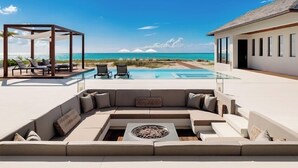 Un espace de vie extérieur moderne, doté d’une piscine, de chaises longues et d’un coin salon abrité offrant une vue sur l’océan.