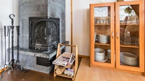 A rustic room with a stone fireplace, a wooden cabinet with glass doors, and a wooden ceiling. - Aurinkoalppi 10a by Interhome (Hyrynsalmi)