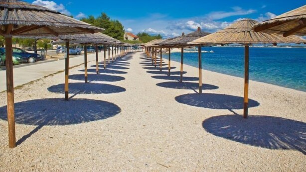 A beach with rows of thatched umbrellas and a clear view of the ocean.