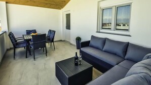A modern living room with a wooden ceiling, a grey sofa, a dining area with chairs, and a window with a view.