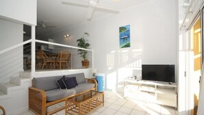 Un salon lumineux, avec un canapé, un téléviseur et un escalier menant à l’étage supérieur.