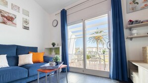 A modern living room with a blue sofa, a small table with a cup and a plant, and a view of a balcony with outdoor furniture. - Wonderful  villa for 6 guests with A/C, pool, WIFI, TV, patio and pets allowed (Deltebre)