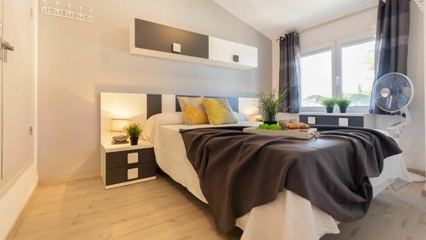 A modern bedroom with a bed, bedside tables, a ceiling fan, a window with curtains, and a small plant on the windowsill. - Wonderful  villa for 6 guests with A/C, pool, WIFI, TV, patio and pets allowed (Deltebre)