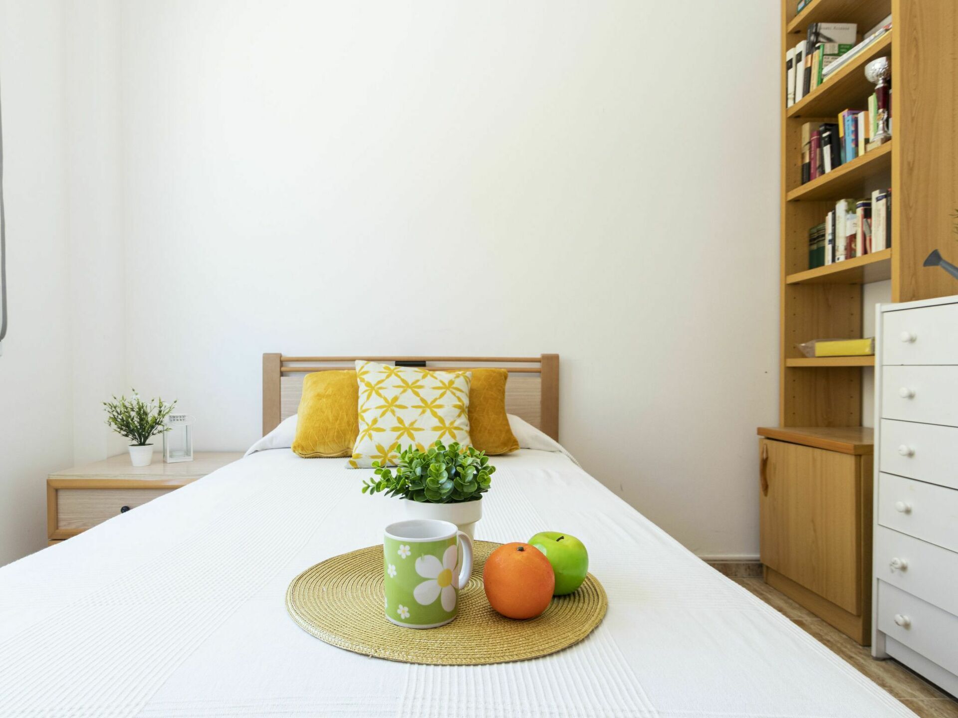 Un dormitorio ordenado con cama, mesita de noche y estantería.