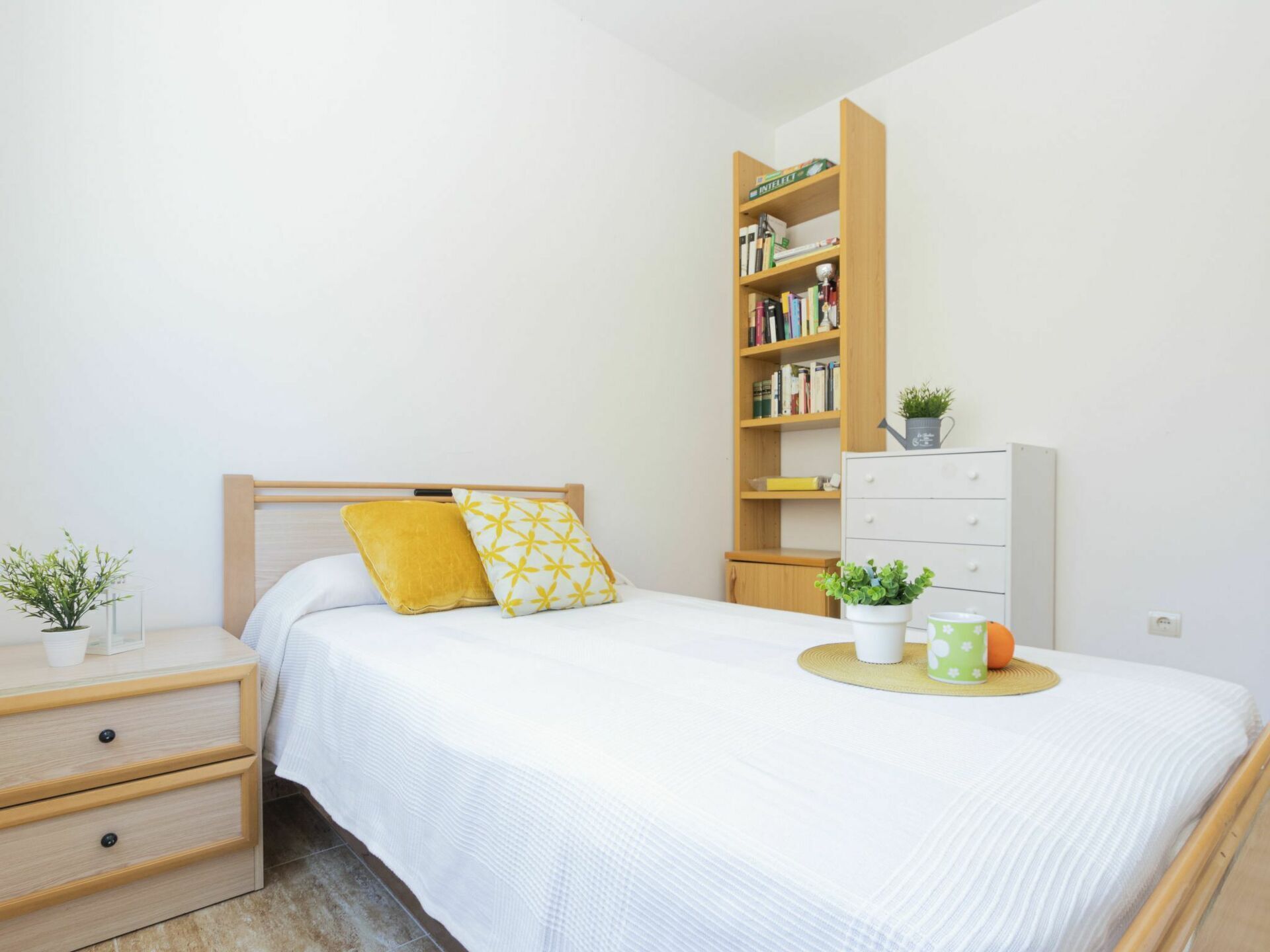 A neatly arranged bedroom with a bed, a nightstand, a bookshelf, and a dresser.
