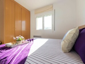 Een slaapkamer met een bed, een houten garderobe, een raam met gordijnen en een dienblad met bloemen.
