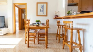 A dining area with a wooden table and chairs, a kitchen in the background, and a framed artwork on the wall. - Beautiful apartment for 4 guests with A/C, WIFI, TV and terrace (L'ampolla)