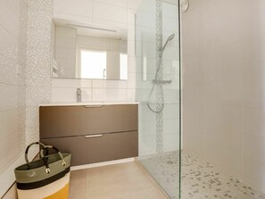 Bathroom features a glass-enclosed shower, handheld showerhead, and wall-mounted controls.