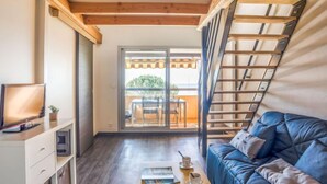 A modern room with a wooden ceiling, a blue leather sofa, a small table with a magazine and cups, and a sliding glass door leading to an outdoor area with a table and chairs. - La Gaillarde by Interhome (Les Issambres)