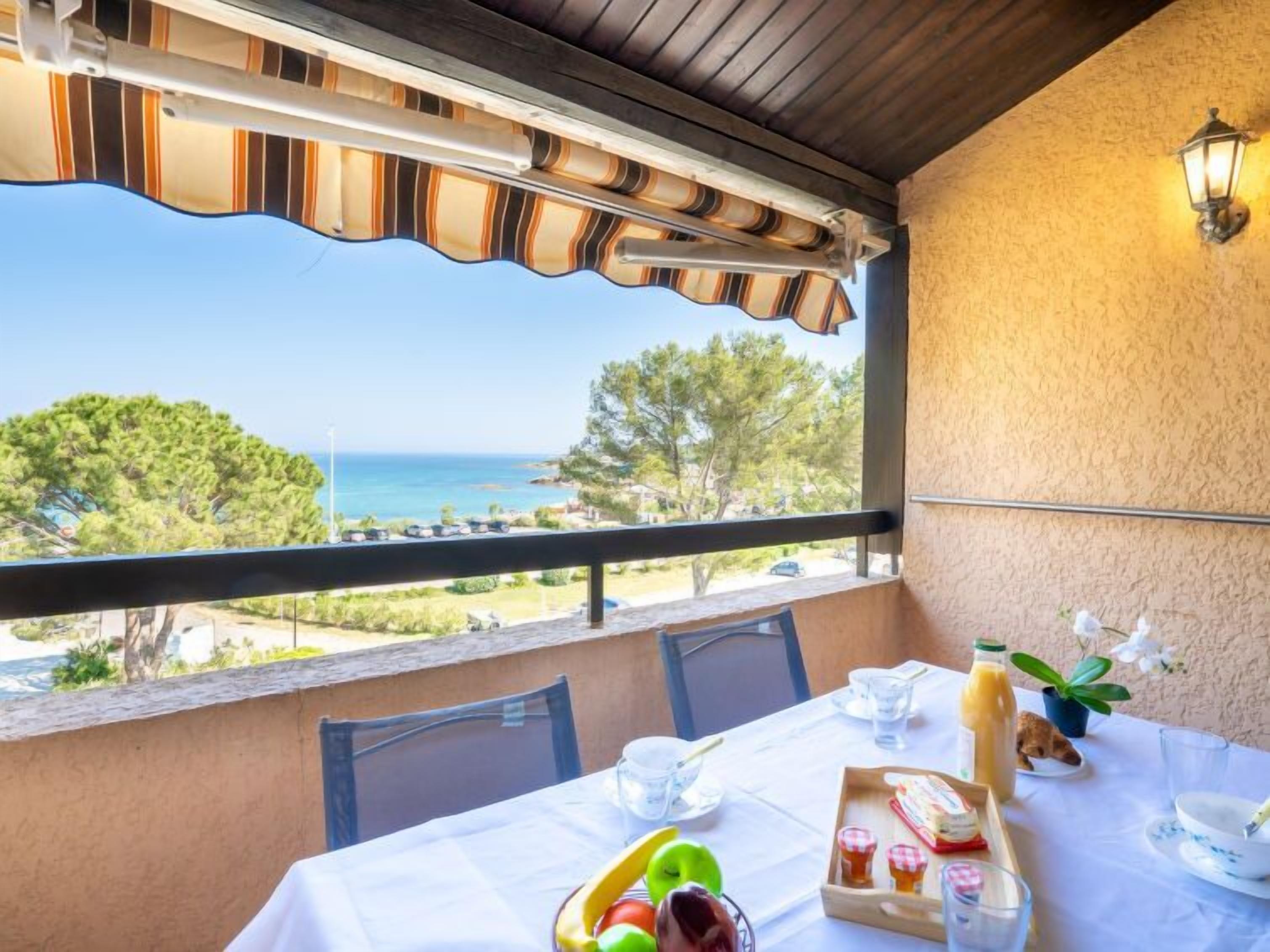 A balcony with a table set for breakfast, overlooking a coastal view.