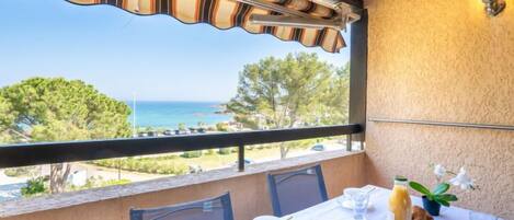 A balcony with a table set for breakfast, overlooking a coastal view.