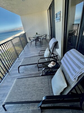 Un balcon avec vue sur l’océan, une table avec des chaises et un coin salon agrémenté d’une serviette à rayures.