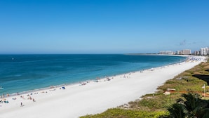 A wide beach with clear blue water, a white sandy shore, and a city skyline in the background. - Upscale Sea Winds 8th Floor Beachfront Weekly Rental (Marco Island)