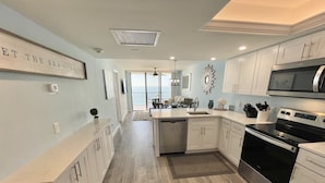 A modern kitchen with white cabinets, stainless steel appliances, and a view to the outside. - Upscale Sea Winds 8th Floor Beachfront Weekly Rental (Marco Island)