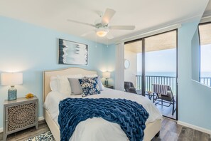 Une chambre à coucher comprenant un lit, un ventilateur de plafond, une table de chevet, une lampe, une horloge et un balcon avec une chaise et une table.